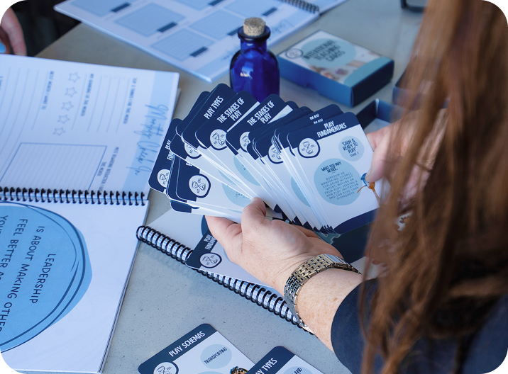 A person holds a fanned stack of blue and white cards over a table with notebooks, a blue bottle, and other stationery items.