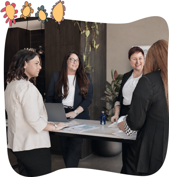 Four women in business attire stand around a table with papers and a laptop, engaged in discussion in a modern office setting. Decorative graphics appear at the top of the image.