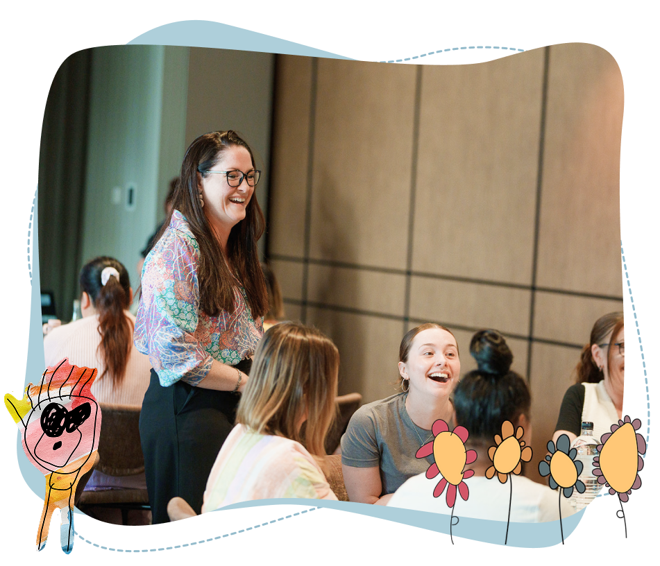 A group of women sit and stand together indoors, smiling and talking; childlike flower and character drawings decorate the image’s border.