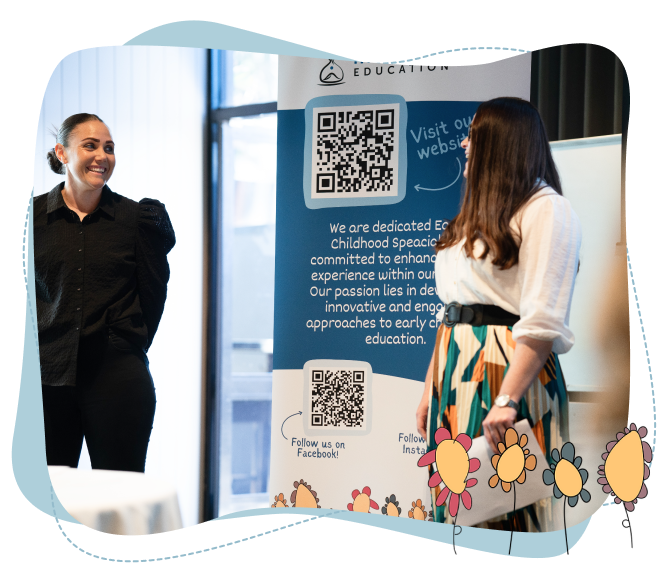 Two women stand and talk in front of a banner with QR codes and social media info about early childhood education, with illustrated flowers at the bottom.