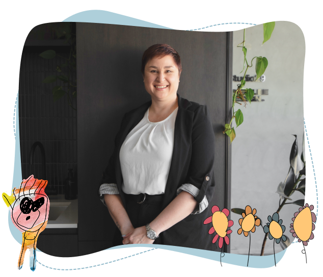 A person in a black blazer and white shirt stands smiling in an office with plant decor. Child-like drawings and flowers frame the image.
