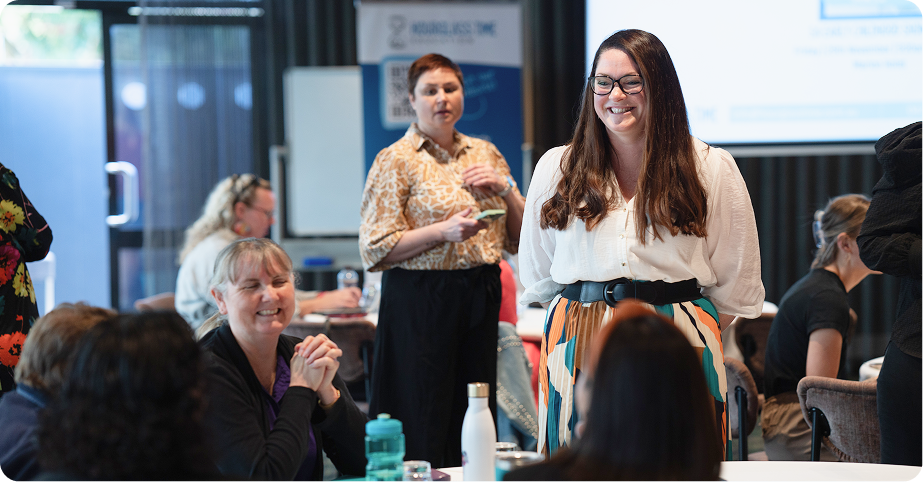 A group of people sit and stand in a bright meeting room, engaging in conversation and smiling during a workshop or seminar.